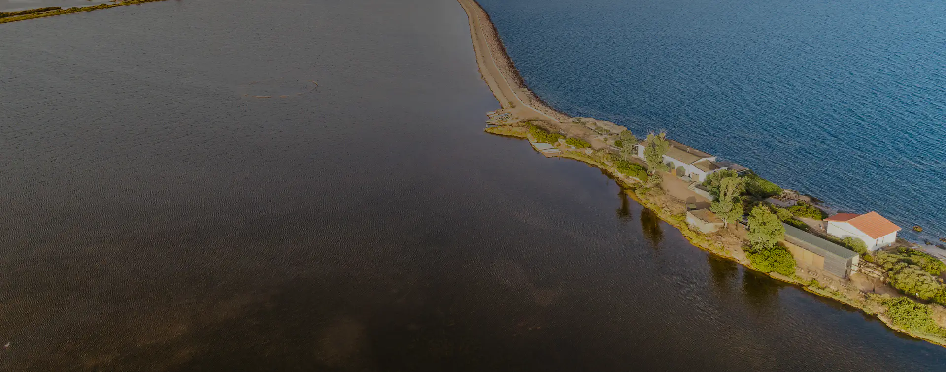 Veduta aerea della Laguna di Nora con le sue acque salmastre e l’istmo che separa la laguna dal mare, dove sorge il centro visite immerso nella natura costiera.