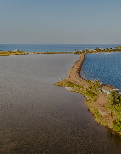 Veduta aerea della laguna di Nora con la lingua di terra che separa mare e parco lagunare Nora, cuore dell’ecosistema lagunare esplorabile con visite guidate.