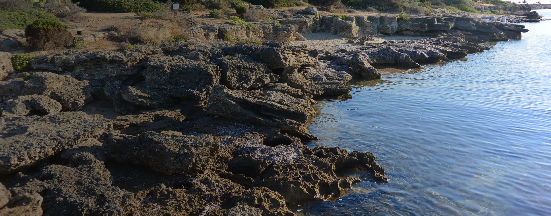 Scogliera affacciata sulla laguna di Nora con acque cristalline e tracce archeologiche.